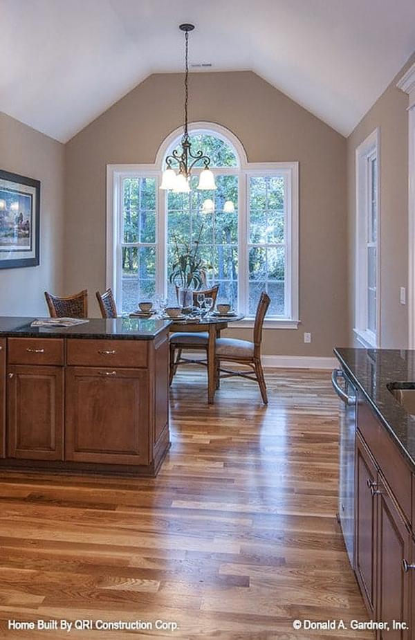 Breakfast nook across the kitchen with a warm chandelier and a round glass top table surrounded by cushioned chairs.