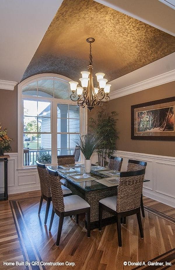 The formal dining room has a barrel-vaulted ceiling and brown walls adorned by a framed artwork and white wainscoting.