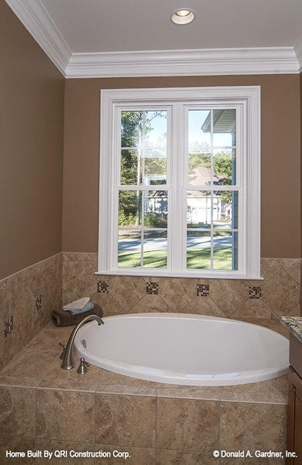 A drop-in tub clad in brown marble tiles and fixed under the white framed window.