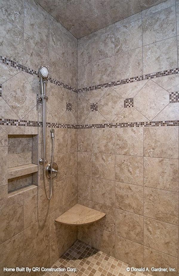 Shower area with mosaic flooring and brown tiled walls fitted with inset shelves and a corner tiled seat.