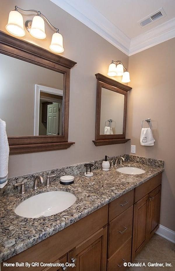 This dual sink vanity has a granite countertop and wooden framed mirrors lit by warm glass sconces.