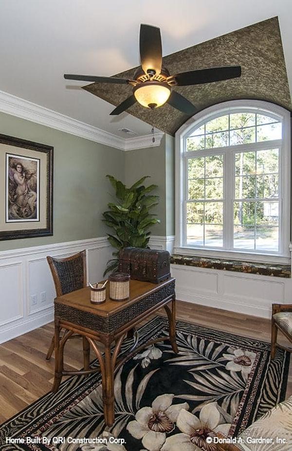 Home office with green and white wainscoted walls, arched window, and hardwood flooring topped with a black floral rug.