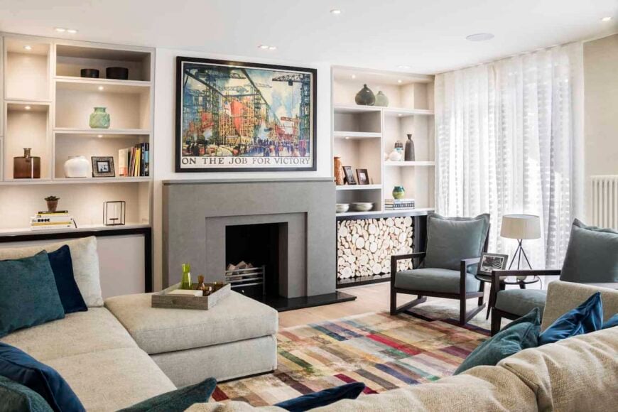 The fireplace is central to the space flanked by custom built-in shelving. The furniture includes a large, comfortable u-shaped sectional sofa facing two wood-framed accent chairs. 