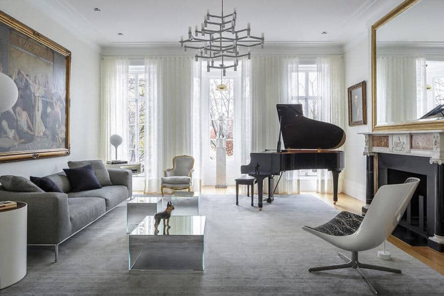 This room also features both modern and historic themed furniture, as well as a large piano set next to the windows. Natural light reflects off multiple surfaces in this space.