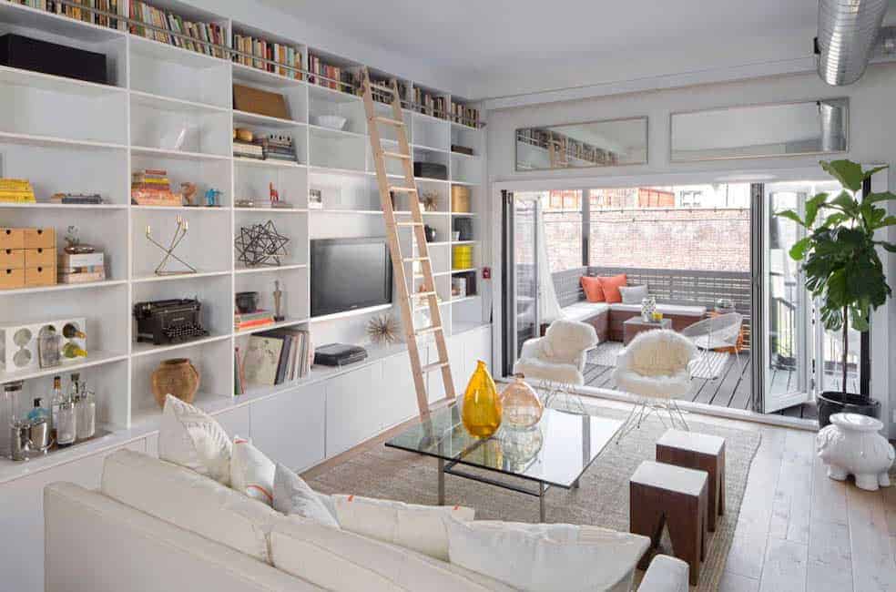This living room features a cozy couch and glass table on the rug and built-in bookshelves with a wooden rolling ladder.