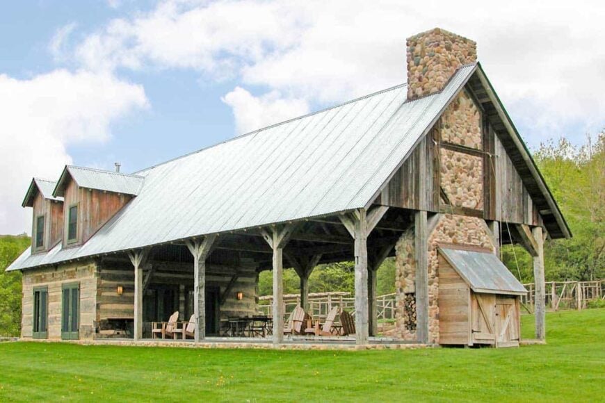 The home's angled side view shows the large outdoor living with a stone fireplace and supported by rustic columns.