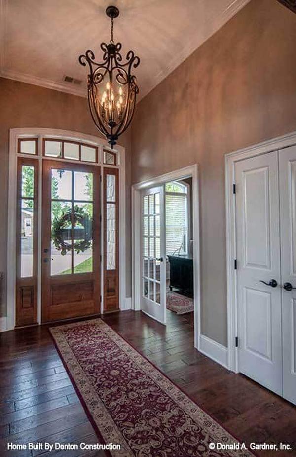 The foyer has a wooden front door and a red classic runner illuminated by an ornate chandelier.