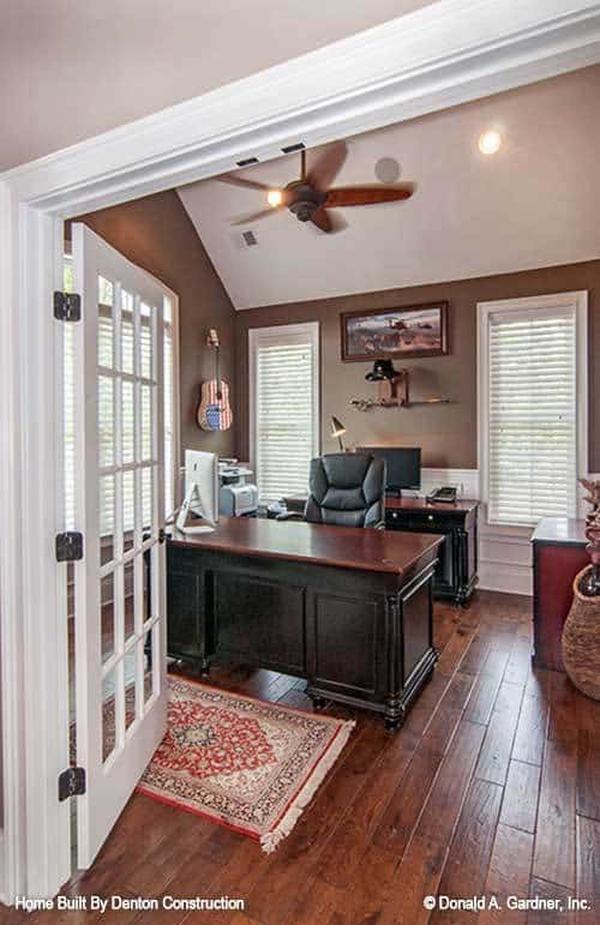 Home office with a white framed door, cathedral ceiling, and brown walls designed with white wainscoting.