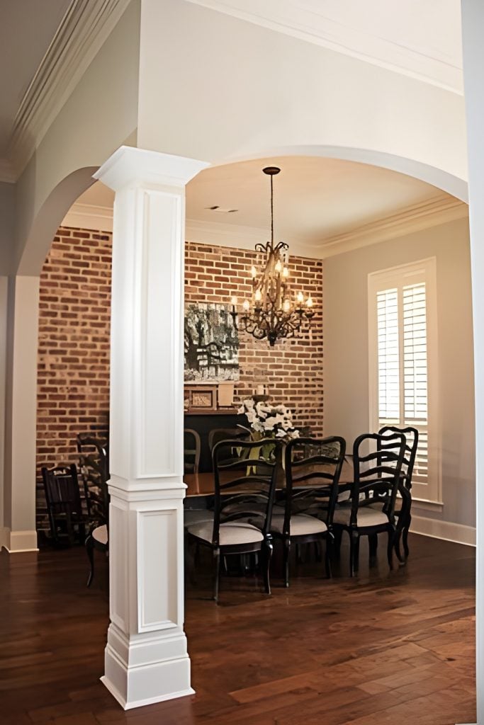 A formal dining room framed with open arches offers a dark wood dining set illuminated by a warm chandelier.