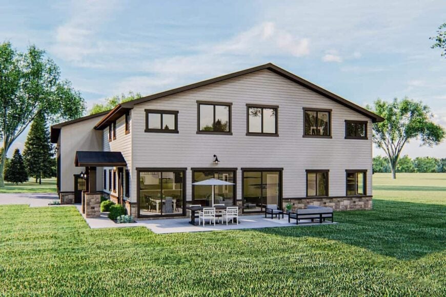 Home's side exterior view with tinted glazed windows and an open patio filled with gray cushioned seats and a wooden dining table under the outdoor umbrella.