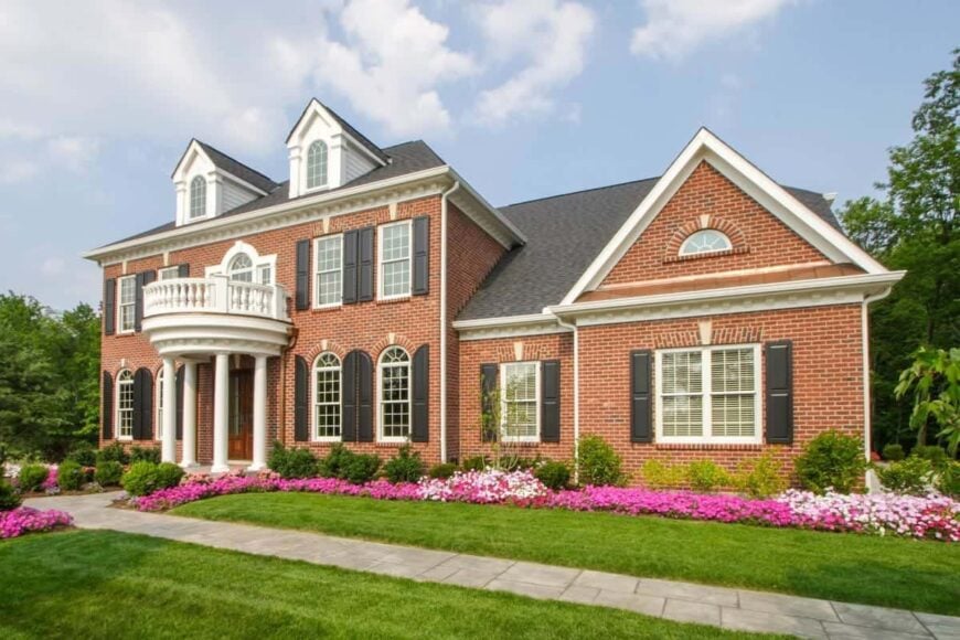 Home's facade with red brick exterior, dormer windows, and a rounded balcony supported by white columns.