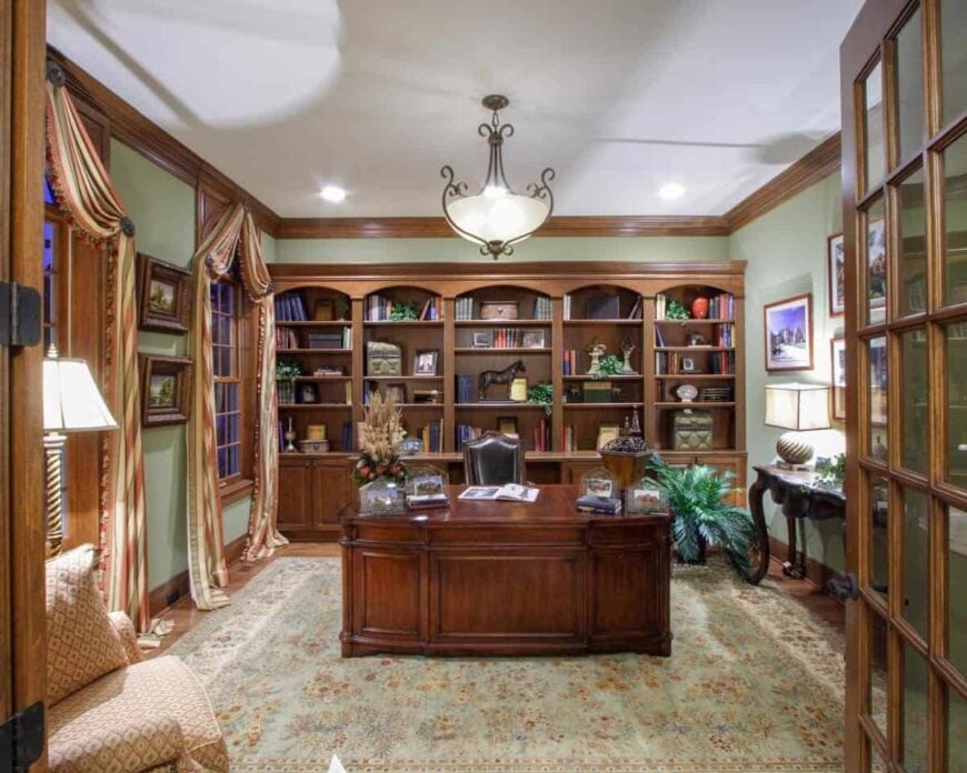 Home's study with a floral area rug, a patterned armchair, and dark wood desks matching with the built-in shelves and cabinets.