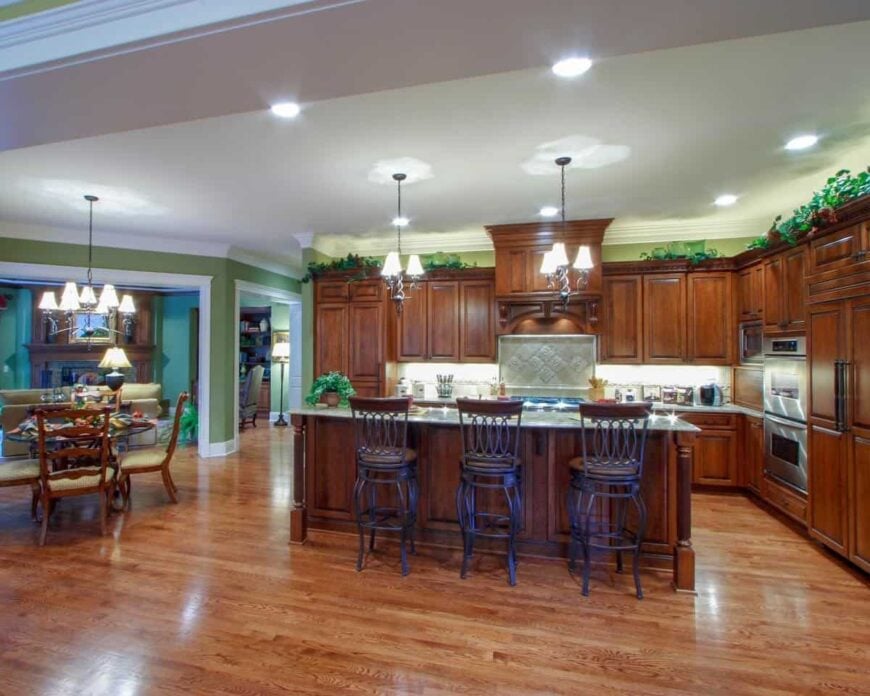 The kitchen next to the breakfast nook is equipped with stainless steel appliances, wooden cabinetry, and a central island lined with matching round stools.