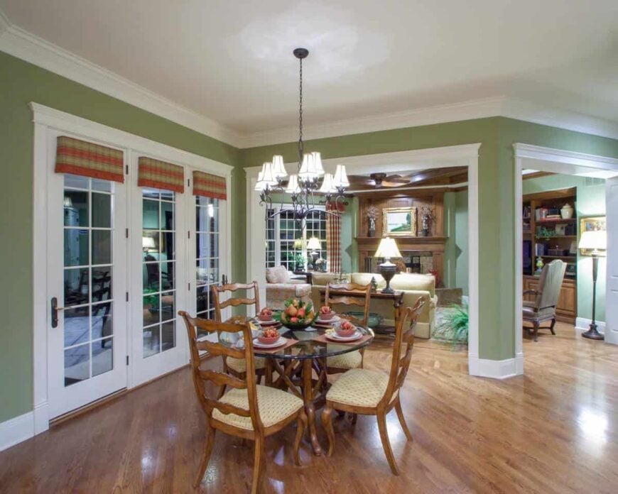 The breakfast nook offers beige cushioned chairs and a round glass top table illuminated by a wrought iron chandelier.