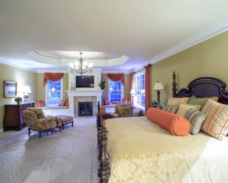 The primary bedroom has a four-poster bed, floral lounge chairs, and a fireplace flanked by window seats.