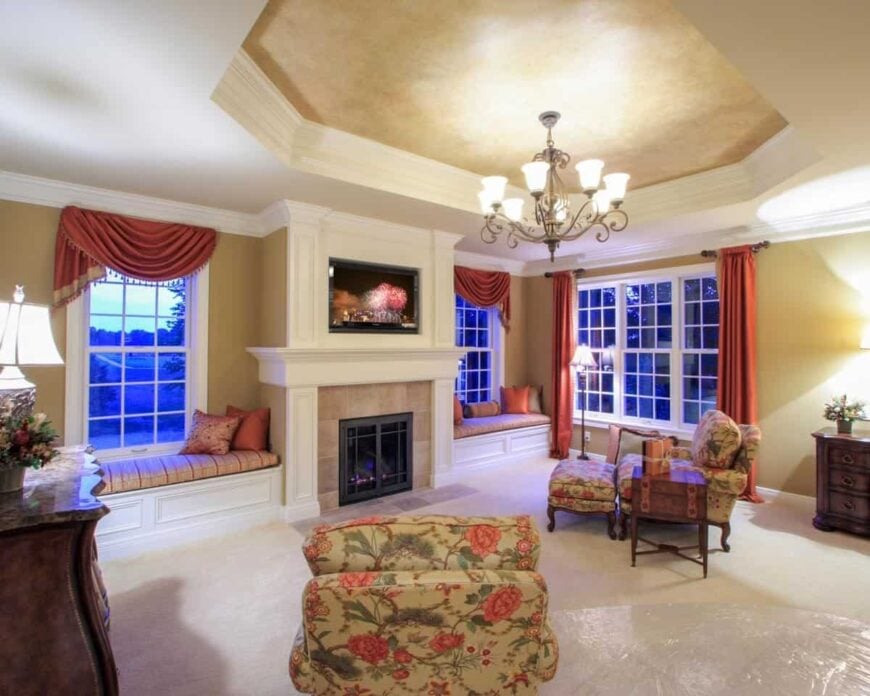 A closer look at the primary's sitting area shows the beige carpet flooring and a tray ceiling mounted with an ornate chandelier.