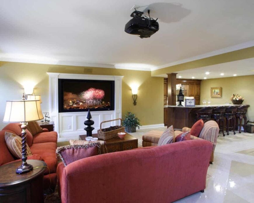 The media room has a wall-mounted screen, red sofas, and a striped chaise lounge surrounding the wooden coffee table.