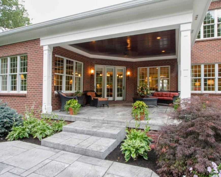 The rear porch is filled with a wicker table and matching seats fitted with red cushions.