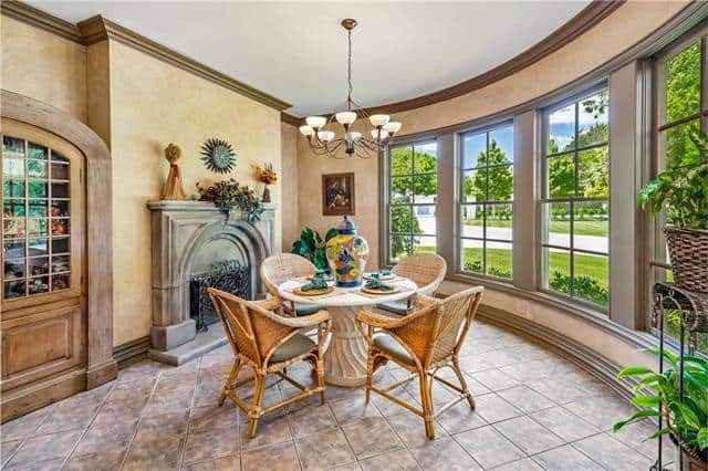 Breakfast nook with a concrete fireplace and round dining set lit by a glass chandelier along with natural light from the framed windows.
