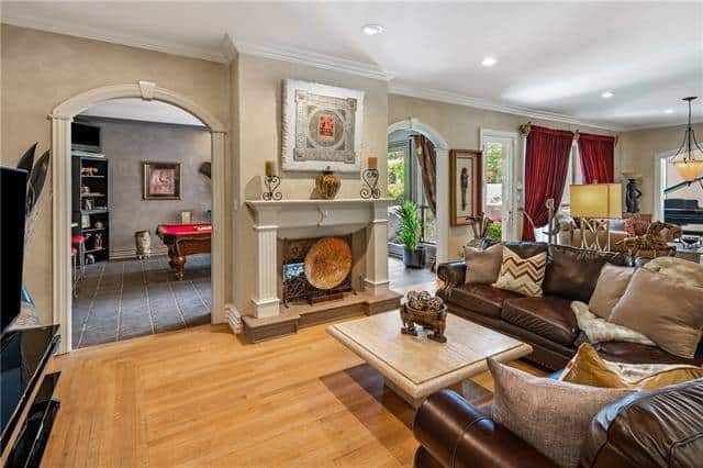 Family room with brown leather sectional and a fireplace nestled in between the archways leading to the game room and patio.
