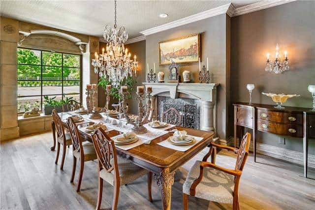 The formal dining room offers a marble fireplace, dark wood buffet and a long dining set illuminated by a warm beaded chandelier.