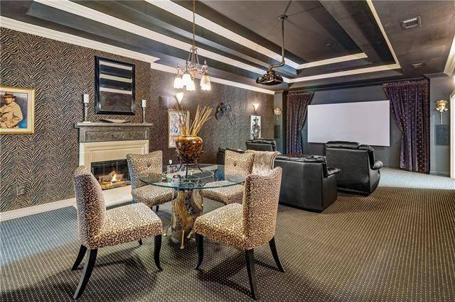 The sitting area behind the black seats showcasing a round glass top table and printed chairs complemented with a fireplace.