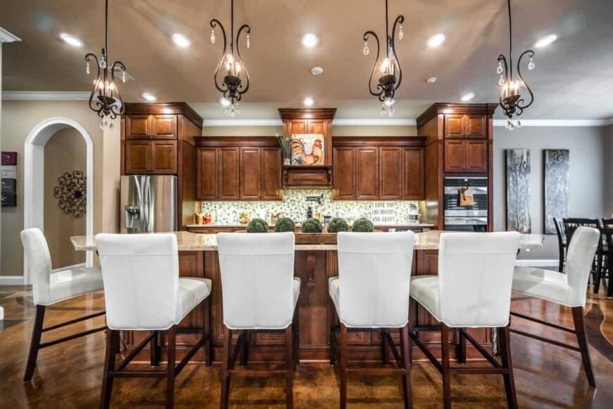 Kitchen with wooden cabinetry and a center island complemented with ornate pendants and white leather counter chairs.