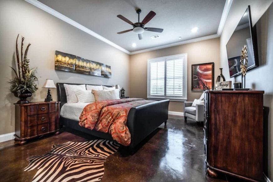 This bedroom offers a black leather bed, gray armchair, a zebra rug, and a wall-mounted TV fixed above the wooden dresser.