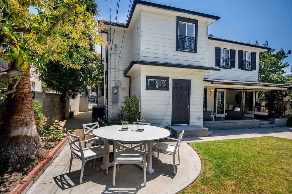 This is a charming patio fitted with an outdoor dining area beside the beauty of the surrounding landscape. It has a concrete floor that connects with the concrete walkway surrounding the grass lawn.
