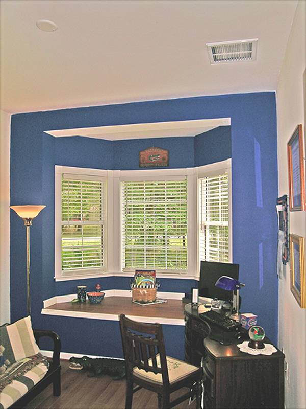 The study offers cushioned chairs, a black desk, and a built-in seat fixed against the bay window.