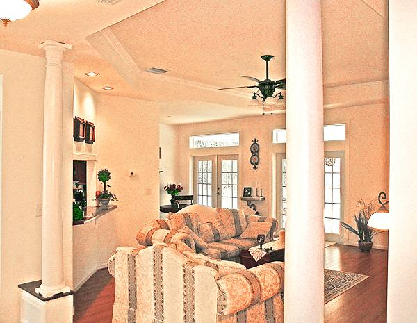 Living room with classy patterned seats and a dark wood coffee table over a printed rug. It is defined with interior columns and a gorgeous step ceiling.