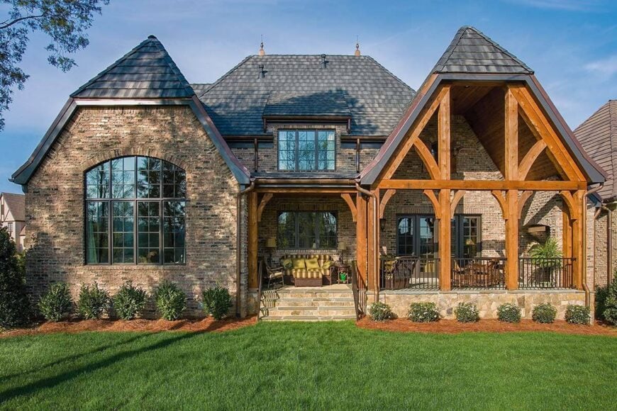 Home's rear view showing the clipped gables, brick exterior walls, and a covered porch framed with natural wood beams.