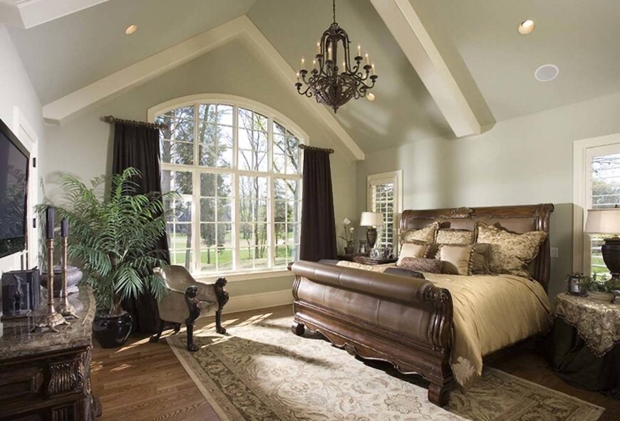 The primary bedroom features a large arched window and a cathedral ceiling lined with white decorative beams.
