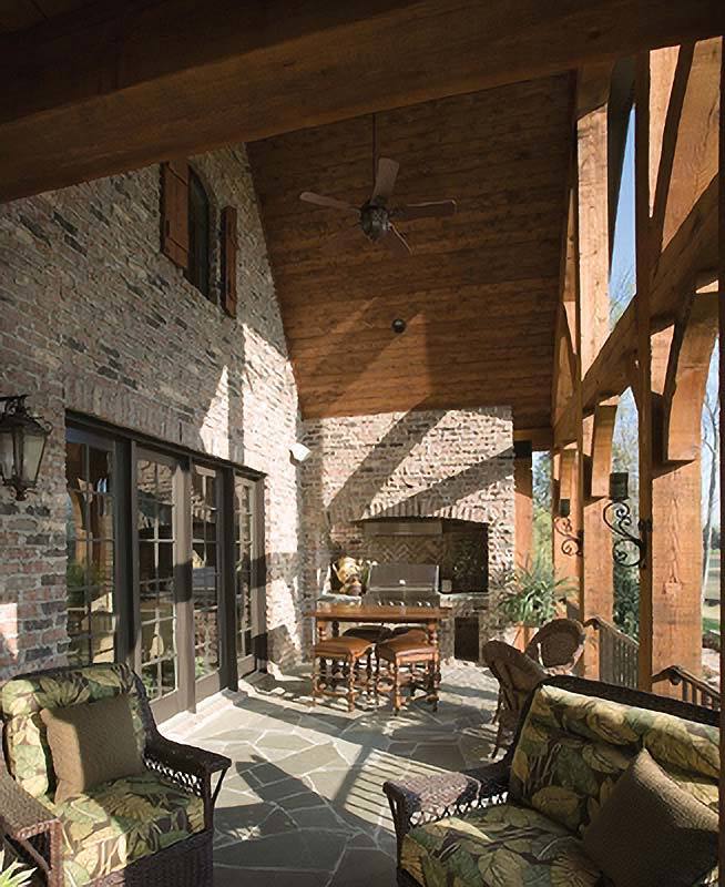 The covered patio has cushioned wicker seats, a wooden dining set, and a summer kitchen fixed against the stone brick walls.