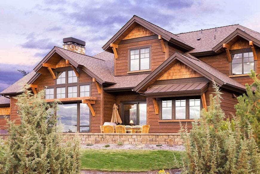 Home's rear view with outdoor living filled with a rectangular dining table and wooden chairs.
