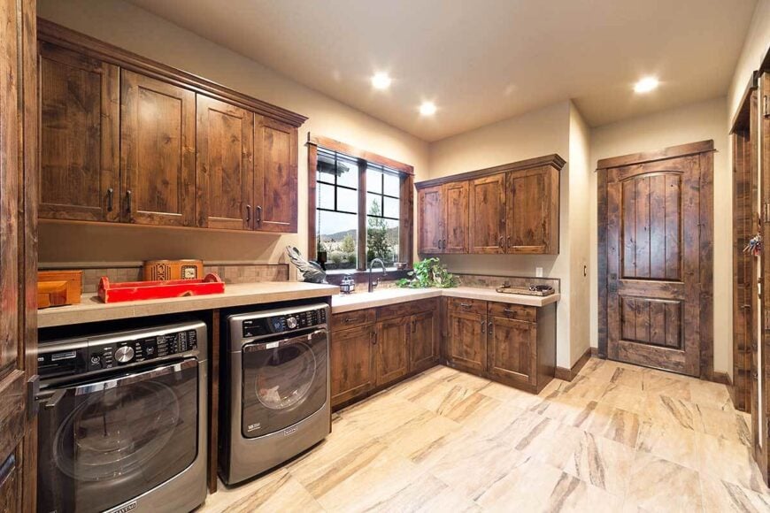 Laundry room equipped with stainless steel appliances and natural wood cabinets that match the rustic door.