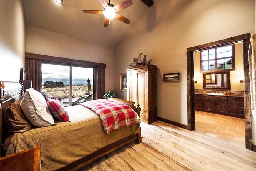 Primary bedroom with a cathedral ceiling, wide plank flooring, and glass sliders that lead to the rear patio.