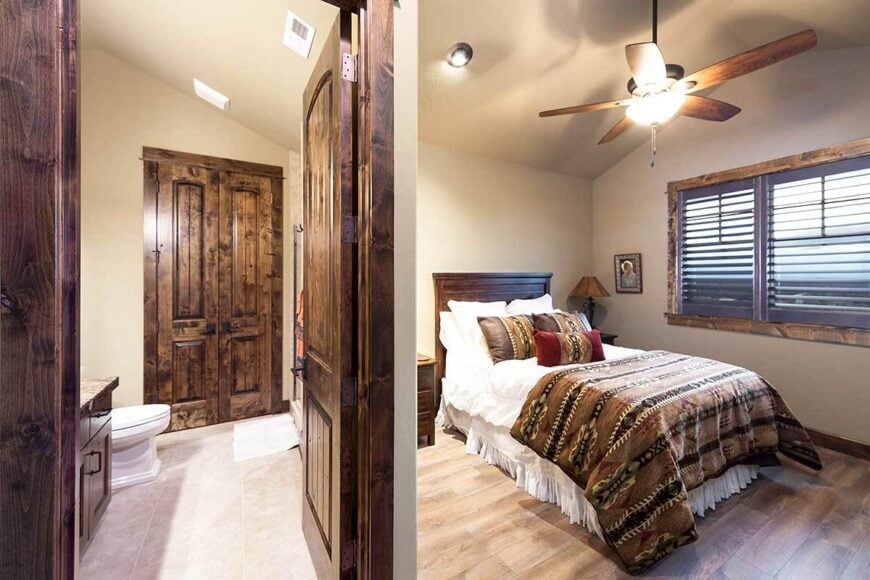 This bedroom has louvered windows and a dark wooden door that opens to the private bath.