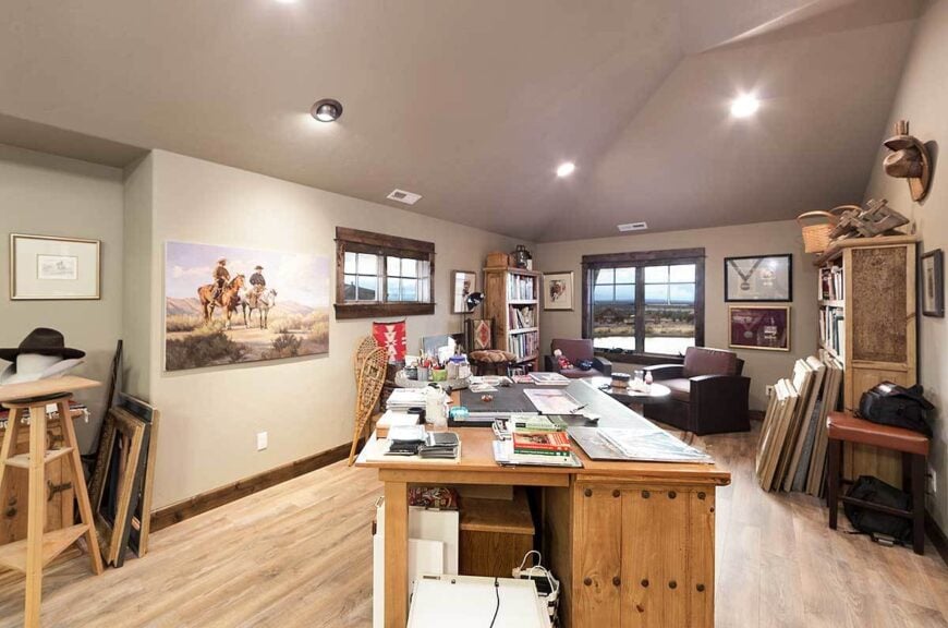 Study with a natural wood desk and a sitting area by the framed window showcasing cozy leather armchairs.