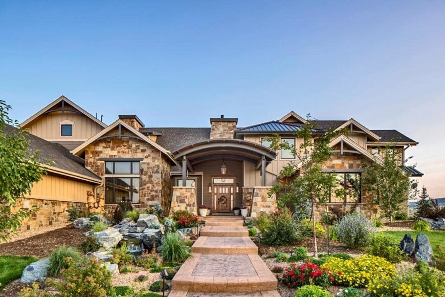A stone layered pathway nestled in between the lush plants. It leads to the home entry lined with stone columns.