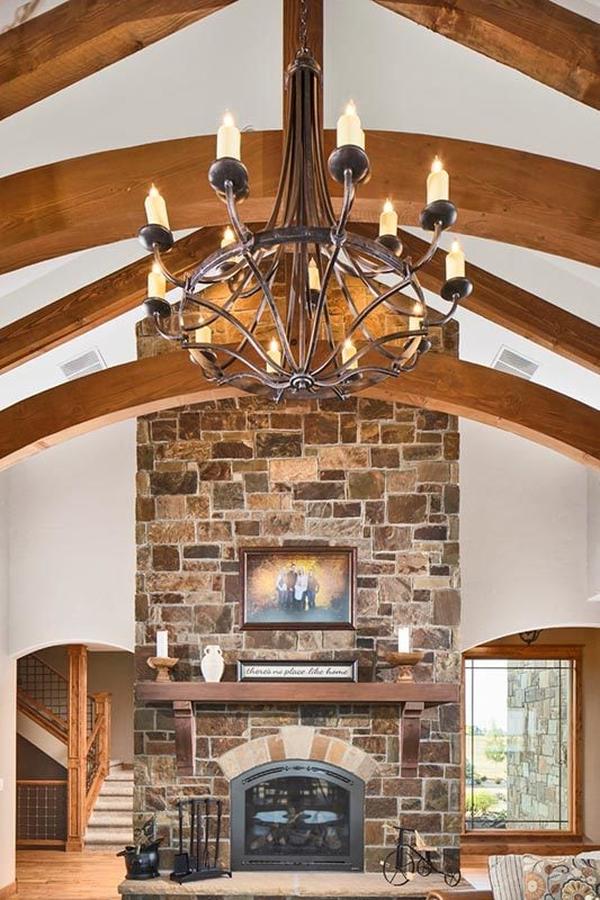 An oversized candle chandelier hanging from the beamed ceiling complements well with the stone fireplace.