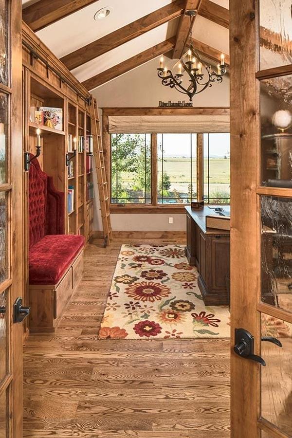 The wooden french door opens to the study with a red tufted seat and a classic desk over a floral area rug.