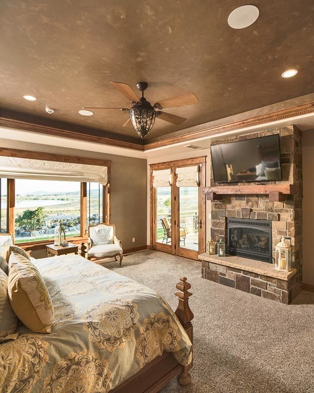 Primary bedroom with a wall-mounted TV, a stone fireplace, a sitting area, and a double door that leads out to the rear deck.