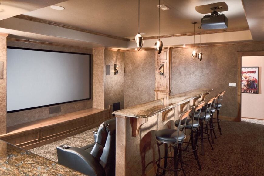 Cozy home theater with black recliners and a granite top bar lined with round bar stools.