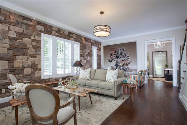 The living room offers a gray sectional sofa, stump tables, and round back armchairs sitting on a floral area rug.