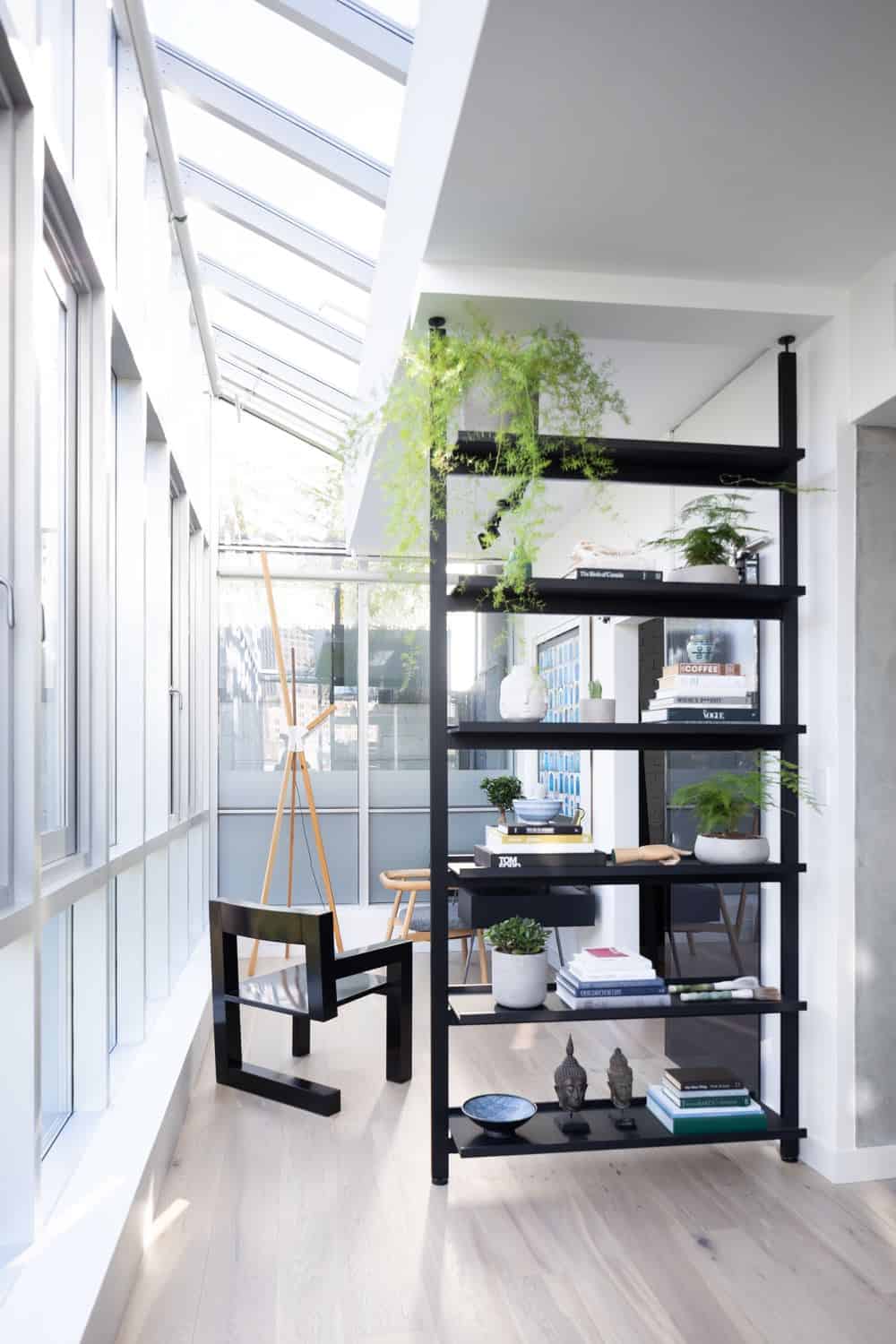 This is a small corner office that makes up for its small floor space with glass walls and skylights. This brightens the white half-ceiling and white wall to be contrasted by the black desk, chairs and shelves.