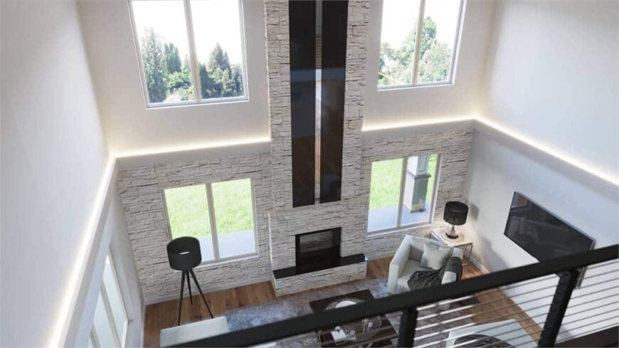 View of the living room from the second-floor balcony showing the gray seats, a dark wood coffee table, and a stone fireplace flanked by glazed windows.