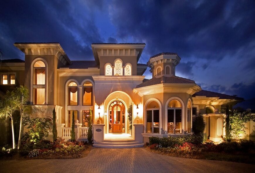 Home's entry showcasing an arched front door flooded by the warm lights of the interior and exterior.