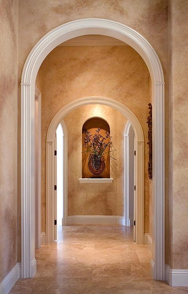An arched hallway with marble walls and an arched inset filled with lovely decor.