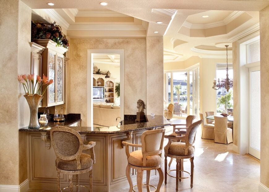 The wet bar offers light wood cabinets and a curved peninsula complemented with round counter chairs.